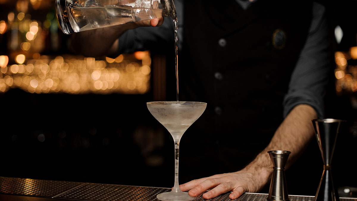 A bartender pouring a cocktail into a chilled glass in a modern speakeasy.