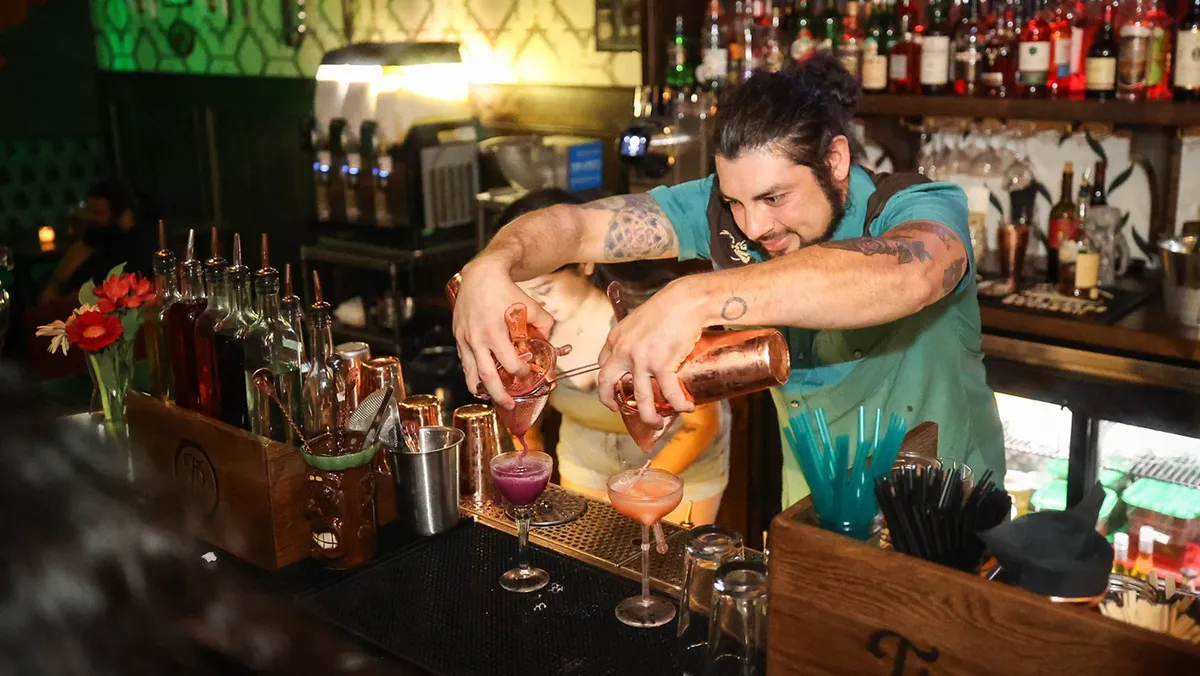 A bartender pouring a cocktail into a chilled glass in a modern speakeasy.
